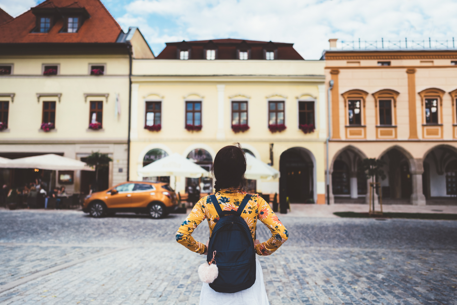A woman with a backpack facing some buildings