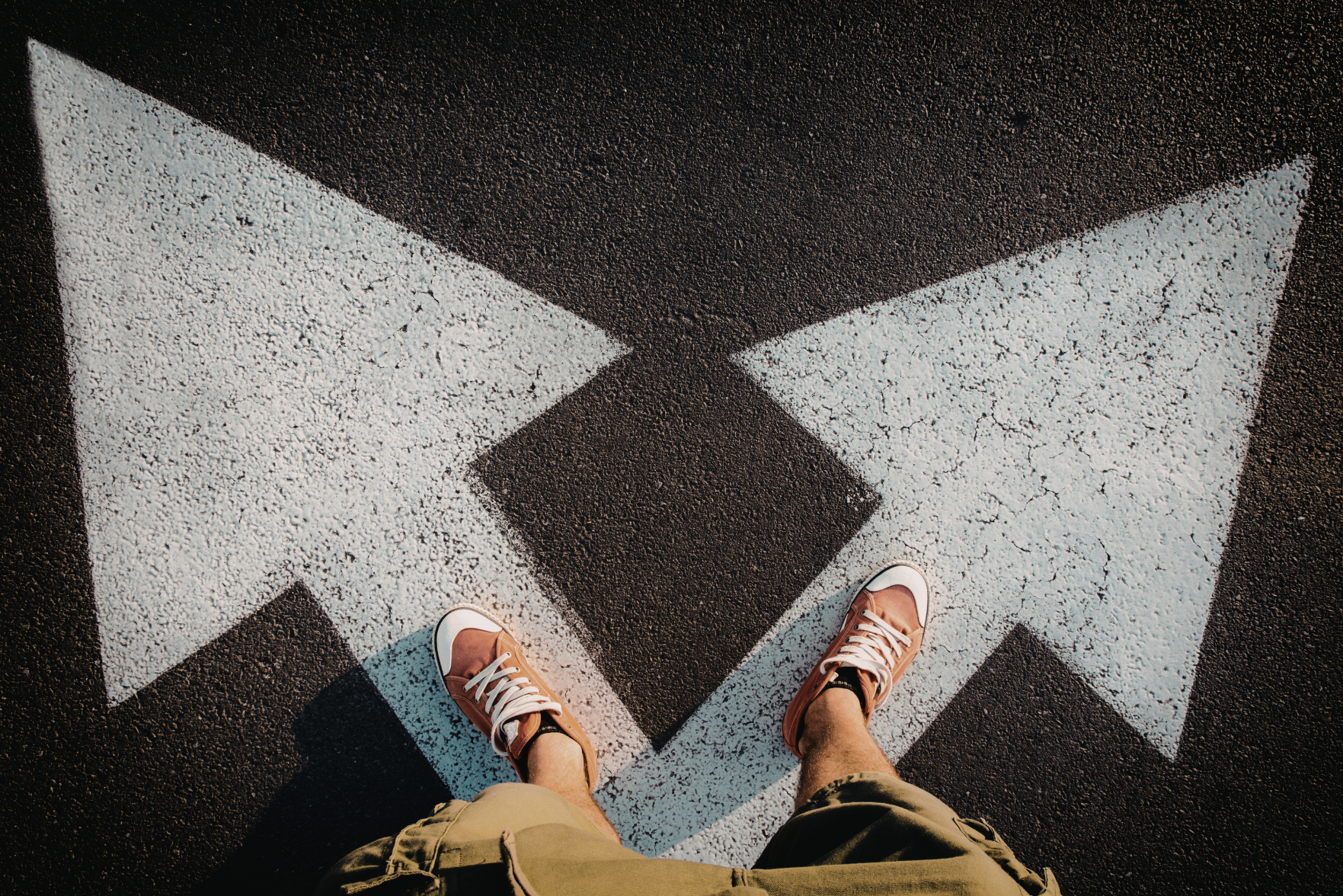 Someone standing on a road with arrows pointing in two directions