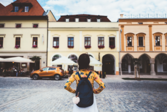 A woman with a backpack facing some buildings