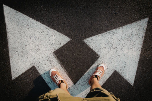 Someone standing on a road with arrows pointing in two directions