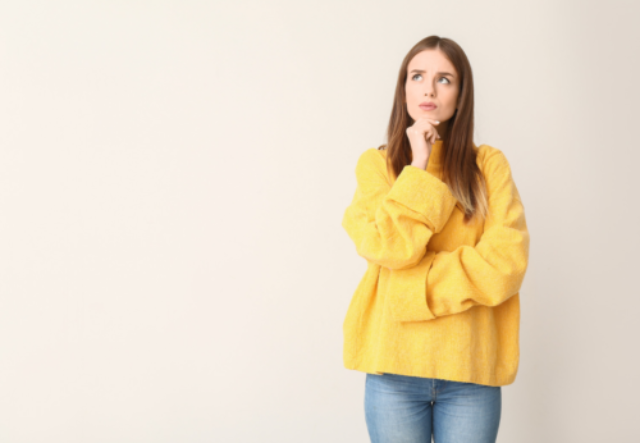 A woman in a yellow jumper considering her options