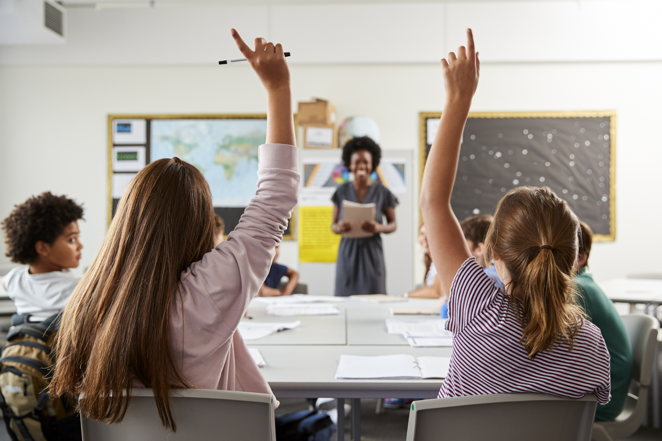 Students in a classroom holding their hands up